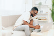 © SHOTPRIME STUDIO - Smiling African American Freelancer Working on Laptop in Modern Home A young African American man is sitting on a comfortable sofa, immersed in his work In a modern and cozy living room, he is typing