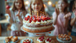 © Neat Design Studio - An adorable young girl holding a birthday cake with strawberries and candles above a table full of treats and desserts with friends cheering in the back