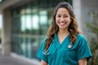 © Dina - hispanic  female nurse intern doctor standing near clinic, smiling in green blue scrubs uniform copy space left