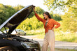 © Home-stock - Young sad woman looking under the hood of her car, automobile broke down and won't start, lady waiting for help