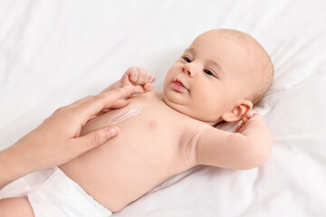 Sticker - Woman applying body cream onto baby`s skin on bed, closeup