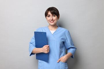 Wall Mural - Portrait of smiling medical assistant with clipboard on grey background