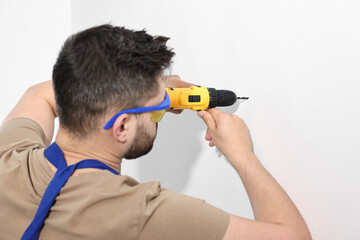 Wall Mural - Young worker in uniform using electric drill indoors