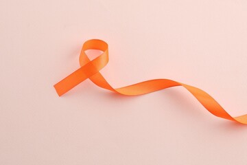 Orange awareness ribbon on beige background, top view