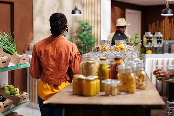 Canvas Print - Black man selling variety of eco friendly, locally grown, and organic products. A customer browses and buys bulk items with reusable packaging, enjoying the freshness approach of the store.