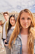 © CarlosBarquero - Vertical. Focus on serious young blonde woman looking at camera on street group multiracial friends in background. Confident people together posing portrait. Gen z colleagues sightseeing on vacation