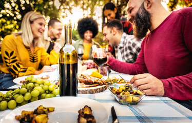 Wall Mural - Happy friends having bbq dinner party in garden restaurant - Cheerful family drinking red wine together sitting at dining table - Food and beverage concept with guys and girls eating fresh meal