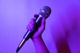Fototapeta Zachód słońca - close-up shot of a hand holding a microphone in purple and pink lights