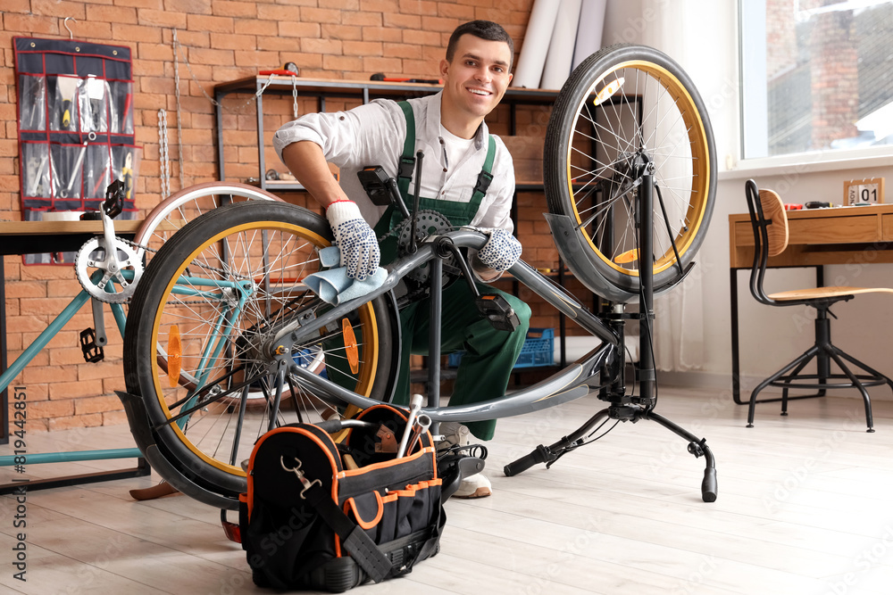 Young mechanic wiping bicycle during repair in workshop