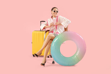 Poster - Happy female office worker in sunglasses sitting on armchair near inflatable ring and suitcase on pink background. Summer vacation concept