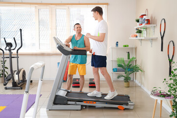 Wall Mural - Male coach with young man training on treadmill in gym