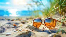 Sunglasses On Sandy Beach Near Ocean Reflecting Sunlight