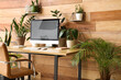© Pixel-Shot - Workplace with blank computer monitor and green houseplants near wooden wall in office