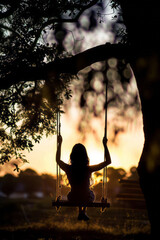 Wall Mural - A silhouette of a girl sitting on a tree swing at sunset creates a backlit image of a young woman swinging in the park.