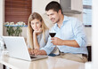 © peopleimages.com - Happy couple, laptop and research with wine glass in kitchen for online shopping, browsing or news at home. Young man and woman with smile on computer for checking renovation or dinner date at house