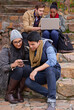 © peopleimages.com - University, laptop or students with phone on campus steps for learning, research or group project planning. Education, college or gen z friends with teamwork for classroom, assignment and support