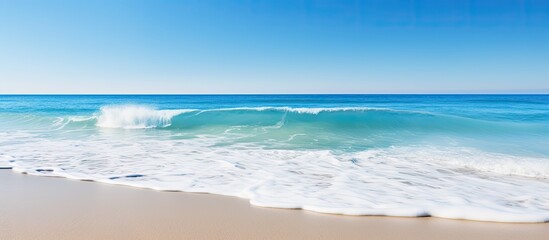 Wall Mural - Scenic view of ocean waves crashing on the sandy beach with a clear blue sky and copy space image in the background