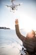 © lightpoet - Young man controlling his drone in snowy outdoors. Drone operator holding a transmitter and landing with a drone.