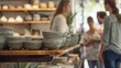 © peera - Matching Bowls Display, Detailed shot of pottery bowls on a shelf, People conversing in the background