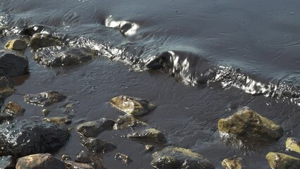 Wall Mural - Closeup of the seashore with calm waves crashing stones on a beach