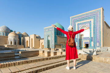 Wall Mural - Young tourist dressed in red with arms raised in front of the Shah-I-Zinda memorial complex in Samarkand, Uzbekistan.