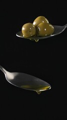 Wall Mural - Olive oil flowing from metal spoon on black background. Food close up, slow motion, vertical video 4K