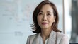 © iuricazac - A poised Asian woman in a professional setting wearing a white blazer and a subtle smile with a blurred map in the background.