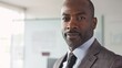 © Z A C - A man with a beard and mustache wearing a suit and tie standing in an office with a window in the background.