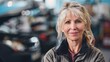 © Z A C - Woman with short blonde hair smiling wearing a black jacket in a blurred automotive workshop background.
