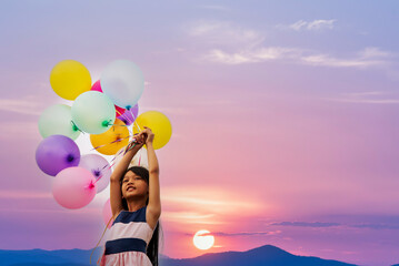 Wall Mural - Cheerful cute girl holding balloons running on green meadow violet purple pastel sky happiness. Hands holding vibrant air balloons play on birthday party happy times summer on pueple sky outdoor