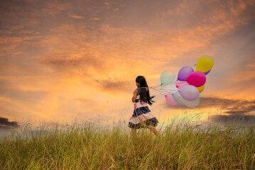 Wall Mural - Cheerful beauty woman holding balloons relax sitting under big tree in green park with happiness. Woman Hands holding vibrant air balloons play on birthday party happy time summer on sunshine outdoor