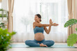 © 220 Selfmade studio - An expectant Asian woman demonstrates a graceful side stretch pose while practicing prenatal yoga in a well-lit promotes flexibility and well-being, essential for a healthy pregnancy