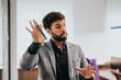 © qunica.com - A confident businessman uses hand gestures to discuss growth strategies during a business meeting in a modern office, standing by a glass wall.