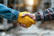 © Kowit - two professionals on a construction site, shaking hands, one with a yellow hard hat, highlighting safety gloves and teamwork.