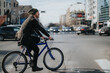 © qunica.com - A young man wearing a beanie pedals a blue bicycle across an urban street with cars and city buildings in the background.