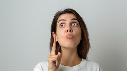 Wall Mural - A young woman with an expressive surprised look, wearing a yellow sweater and pointing upward, standing against a plain background..