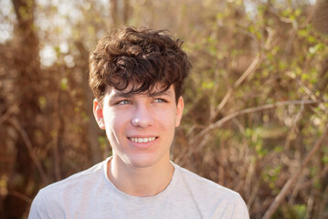 A young teenager boy sincerely smiles and rests in nature in the forest, looks into the distance and dreams about the future. The boy has healthy white teeth