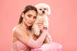 © Dimid - A young beautiful girl in a pink dress with a white small dog on a pink background.