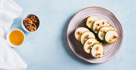 Wall Mural - Pieces of pear, ricotta, honey and nuts on rye bruschettas on a plate top view web banner