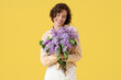 © Pixel-Shot - Beautiful young woman with bouquet of blooming lilac flowers on yellow background