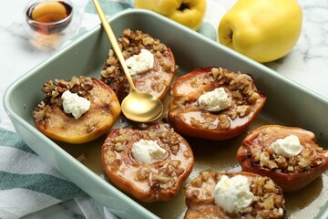 Tasty baked quinces with nuts and cream cheese in dish on table, closeup