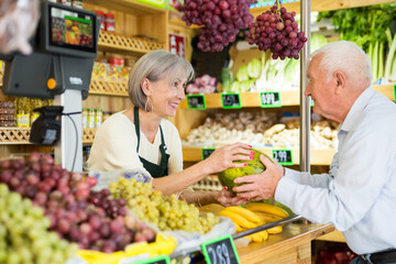 Wall Mural - Woman supermarket employee hands watermelon to an elderly man after paying for purchase at the checkout