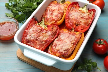 Wall Mural - Tasty stuffed peppers in dish and ingredients on light blue wooden table, closeup