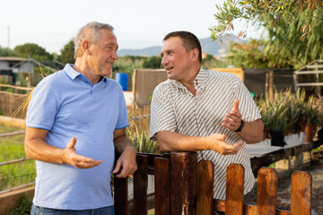 Wall Mural - Cheerful male neighbors standing at fence outdoors and having conversation. Village residents talking outdoors.