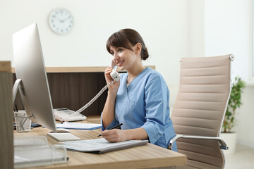 Wall Mural - Smiling medical assistant talking by phone in office