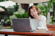 © Satori Studio - A woman is sitting at a table with a laptop and a stack of books. She is looking at the laptop and she is in a state of exhaustion