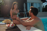 Fototapeta  - Two people drinking cold juice in a pool next to a bowl of fruit