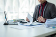 © Wasana - A man in a suit is sitting at a desk with a laptop and a stack of papers