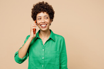 Wall Mural - Young smiling cheerful woman of African American ethnicity wears green shirt casual clothes talk speak on mobile cell phone isolated on plain pastel light beige background studio. Lifestyle concept.