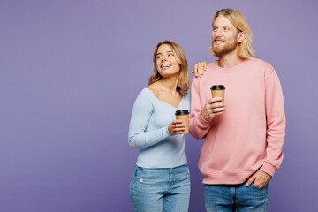 Wall Mural - Young couple two friends family man woman in pink blue casual clothes together hold takeaway delivery craft paper brown cup coffee to go look aside on area isolated on pastel plain purple background